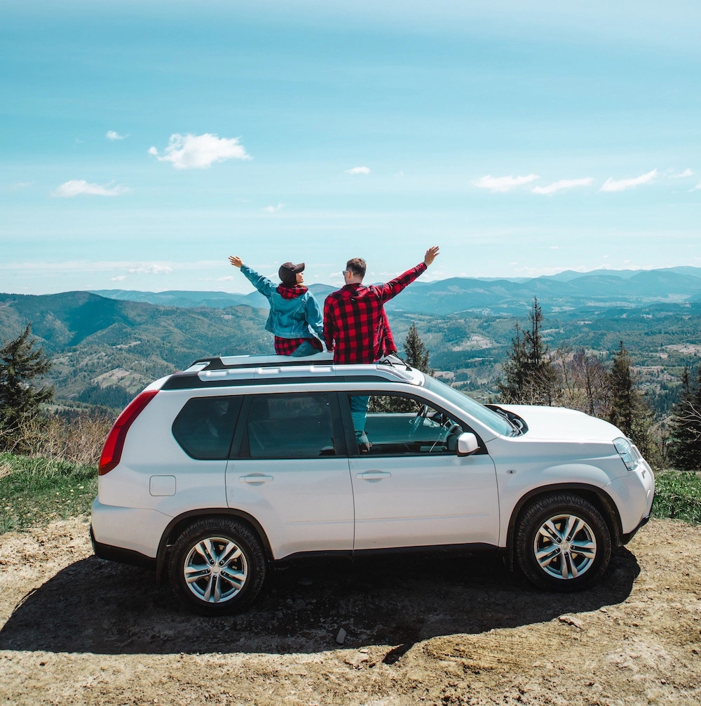 Couple assis sur un 4x4 blanc face aux montagnes, profitant d’un road trip au Costa Rica sous un ciel bleu dégagé.