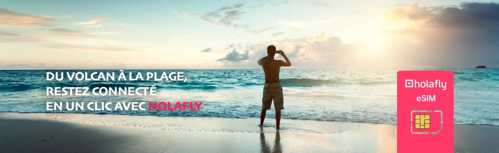 Homme prenant une photo au bord de l’océan au Costa Rica au coucher du soleil, illustrant la liberté de rester connecté avec une eSIM Holafly.